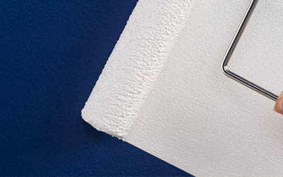 white primer rolling over a blue wall hiding dark colors